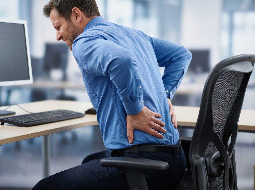 Man experiencing lower back pain and stiffness while sitting at work in New Paltz NY